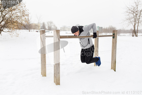 Image of young man exercising on parallel bars in winter