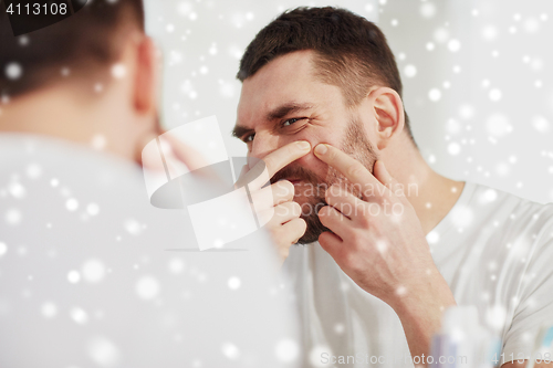 Image of man squeezing pimple at bathroom mirror