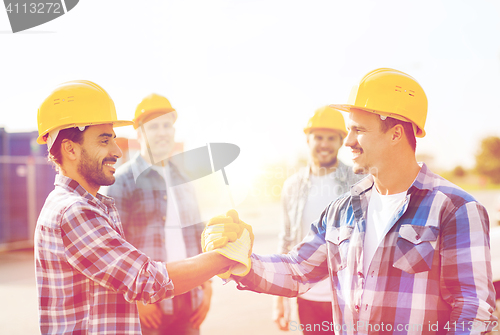 Image of group of smiling builders shaking hands outdoors