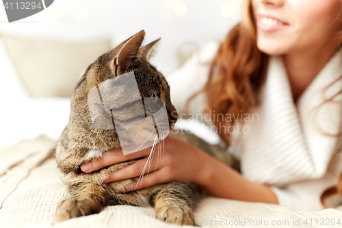 Image of happy young woman with cat lying in bed at home