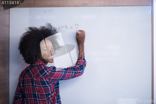 Image of African American woman writing on a chalkboard in a modern offic