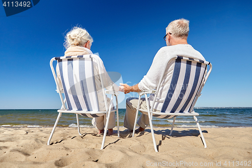 Image of senior couple sitting on chairs at summer beach