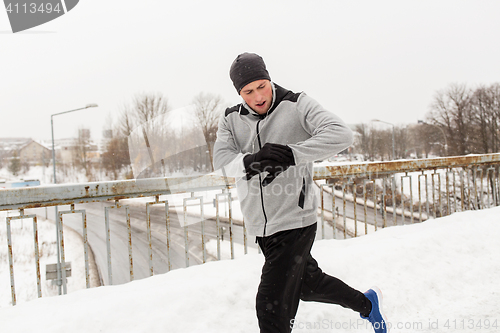 Image of man with earphones running along winter bridge