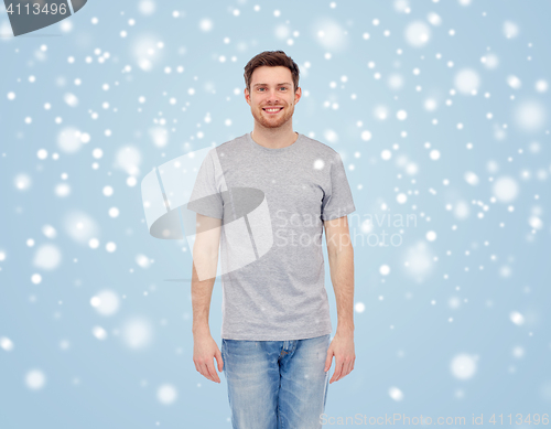 Image of smiling young man in t-shirt and jeans over snow