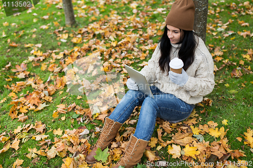 Image of woman with tablet pc and coffee in autumn park