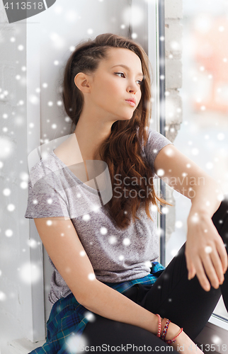 Image of sad pretty teenage girl sitting on windowsill