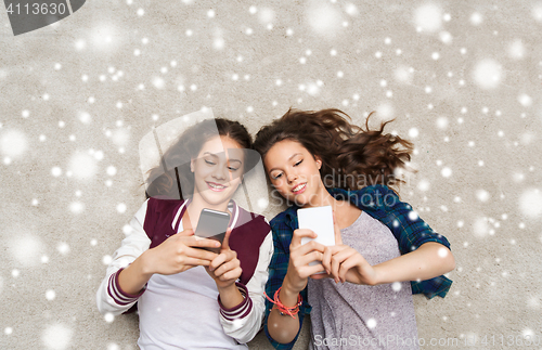 Image of happy teenage girls lying on floor with smartphone