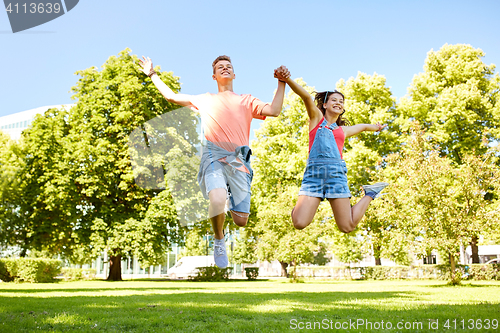 Image of happy teenage couple jumping at summer park