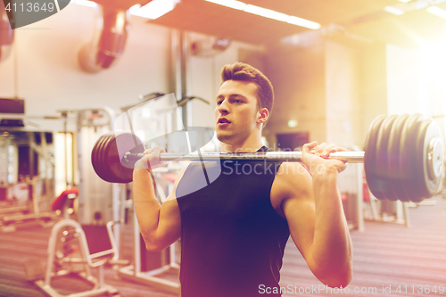 Image of young man flexing muscles with barbell in gym