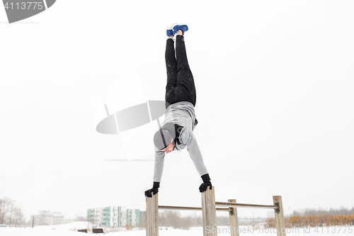 Image of young man exercising on parallel bars in winter