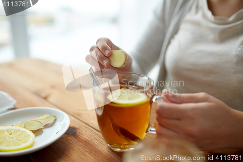 Image of close up of woman adding ginger to tea with lemon