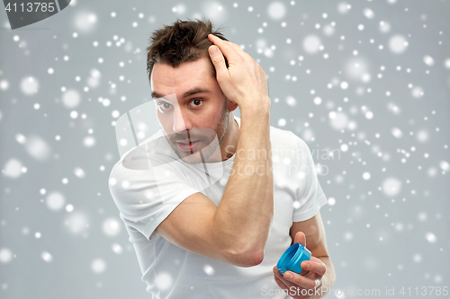 Image of happy young man styling his hair with wax or gel