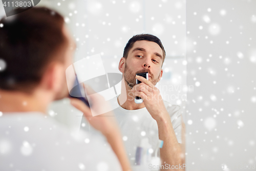 Image of man shaving mustache with trimmer at bathroom
