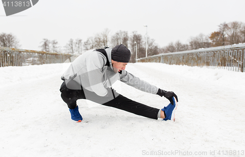 Image of man exercising and stretching leg on winter bridge