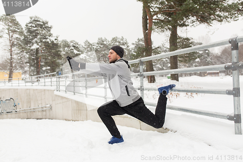 Image of sports man stretching leg at fence in winter