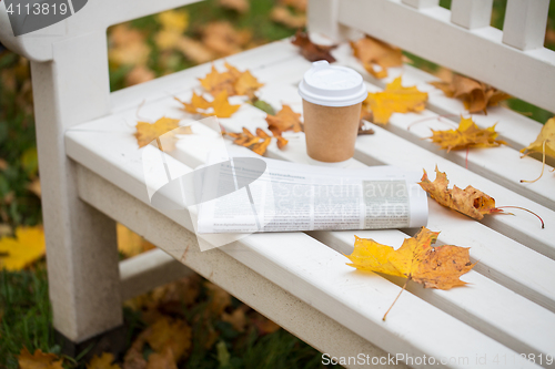 Image of newspaper and coffee cup on bench in autumn park