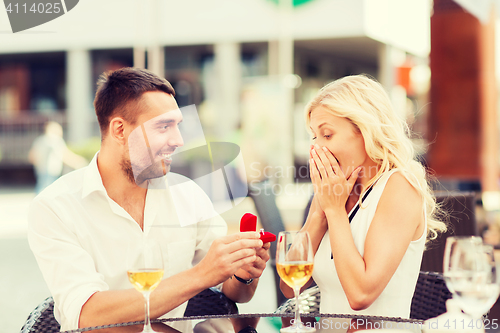 Image of happy couple with engagement ring and wine at cafe