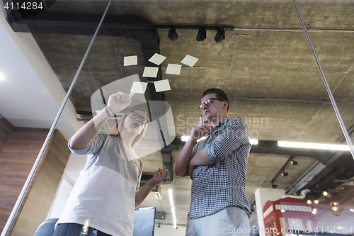 Image of young couple at modern office interior writing notes on stickers