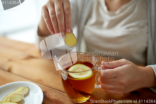 Image of close up of woman adding ginger to tea with lemon