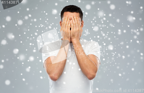 Image of man covering his face with hands over snow