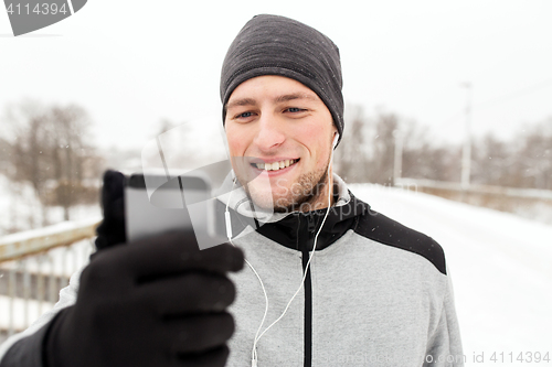 Image of happy man with earphones and smartphone in winter