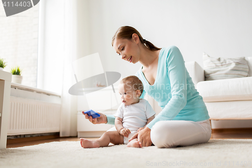 Image of happy mother showing smartphone to baby at home