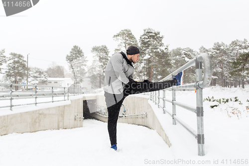 Image of sports man stretching leg at fence in winter