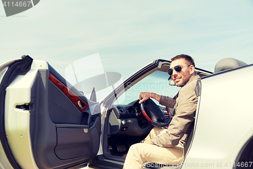 Image of happy man opening door of cabriolet car outdoors