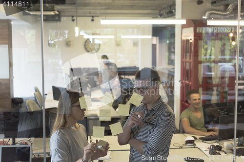 Image of young couple at modern office interior writing notes on stickers