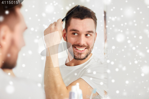 Image of happy man brushing hair with comb at bathroom