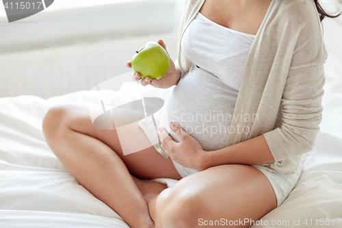 Image of close up of pregnant woman eating apple at home