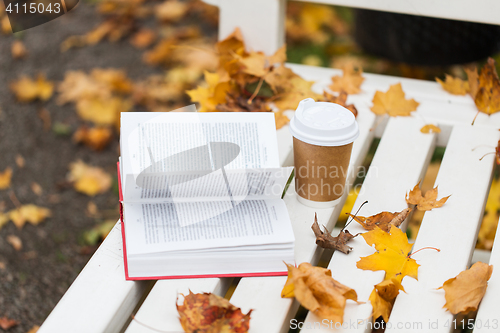 Image of open book and coffee cup on bench in autumn park