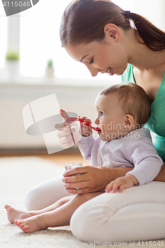 Image of happy mother with spoon feeding baby at home