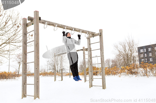 Image of young man exercising on horizontal bar in winter