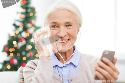 Image of senior woman with smartphone and earphones at home