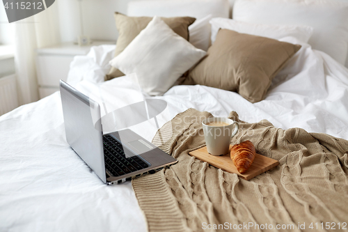 Image of laptop, coffee and croissant on bed at cozy home