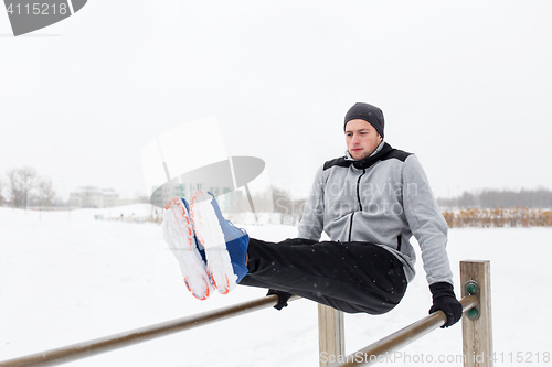 Image of young man exercising on parallel bars in winter