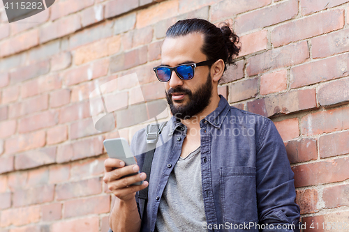 Image of man with backpack texting on smartphone in city