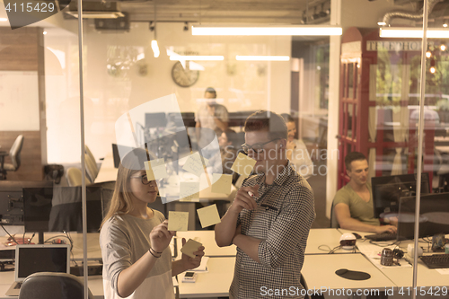 Image of young couple at modern office interior writing notes on stickers