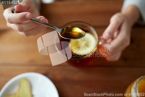 Image of close up of woman adding honey to tea with lemon