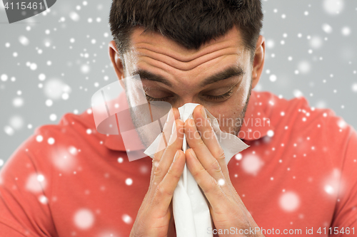 Image of sick man with paper wipe blowing nose over snow