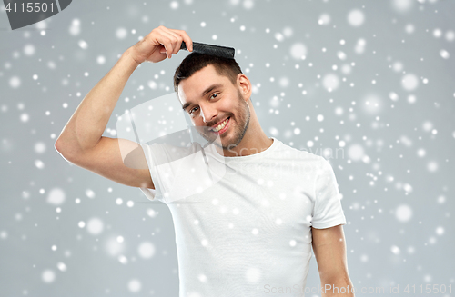 Image of happy man brushing hair with comb over snow