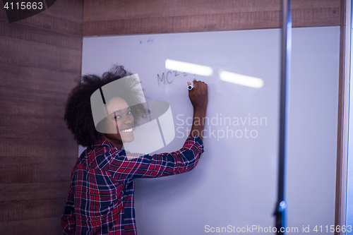 Image of black  woman writing on a white board  in a modern office