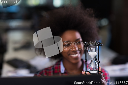 Image of young woman at office looking at sand  clock