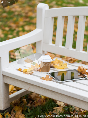 Image of tablet pc and coffee cup on bench in autumn park