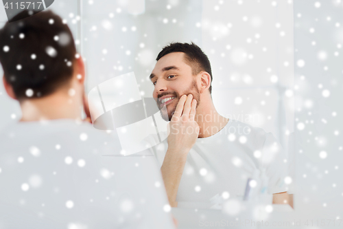 Image of happy young man applying cream to face at bathroom