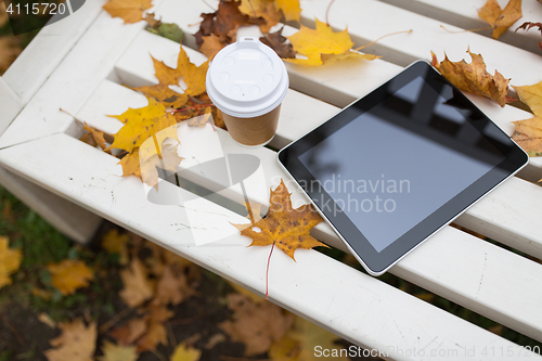 Image of tablet pc and coffee cup on bench in autumn park