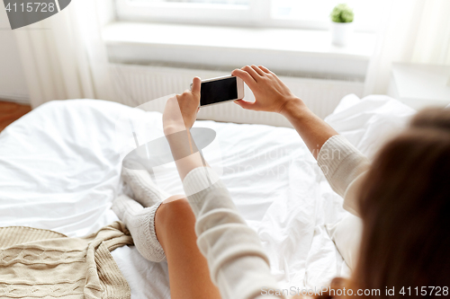 Image of woman photographing with smartphone in bet at home