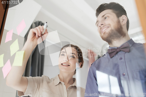 Image of happy creative team writing on blank office glass
