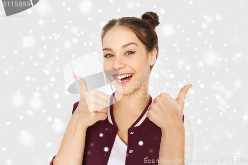 Image of happy teenage girl showing thumbs up over snow